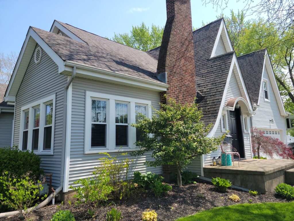 White-trimmed windows on a gray-sided home beside a tall brick chimney