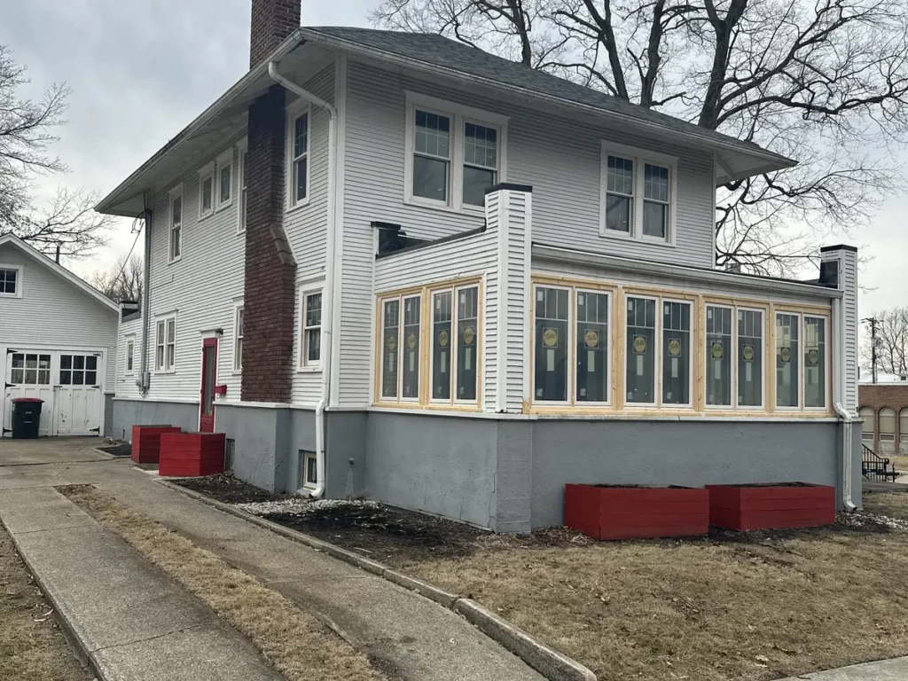 Windows around an enclosed porch on a two-story Attica home with white siding and a brick chimney